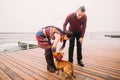 Young happy couple walking with dog on the rainy berth in autumn. Sea background Royalty Free Stock Photo