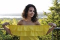 Young happy curly dark-haired girl in a yellow dress with bare shoulders