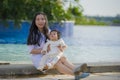 Young happy and cute Asian Chinese woman playing with daughter baby girl at holidays tropical resort swimming pool enjoying summer