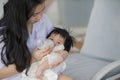 Young happy and cute Asian Korean woman nursing daughter baby girl with formula bottle at holidays tropical resort swimming pool