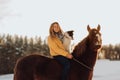 Young happy cute smiling woman with her dog border collie sit on horse in snow field on sunset. yrllow dress Royalty Free Stock Photo