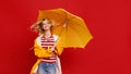 Young happy emotional cheerful girl laughing with yellow umbrella on colored red background