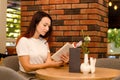 Young happy european girl with brown hair sitting in a cafe near a brick wall reading book at the table Royalty Free Stock Photo