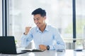 Young happy and excited asian businessman cheering with his fists working on a laptop sitting in an office alone at work Royalty Free Stock Photo