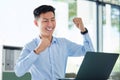 Young happy and excited asian businessman cheering with his fists working on a laptop sitting in an office alone at work Royalty Free Stock Photo