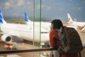 Young happy and excited Asian Chinese student woman with backpack at airport departure lounge watching aircraft through glass Royalty Free Stock Photo