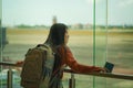 Young happy and excited Asian Chinese student woman with backpack at airport departure lounge watching aircraft through glass Royalty Free Stock Photo