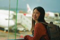 Young happy and excited Asian Japanese student woman with backpack at airport departure lounge watching aircraft through glass Royalty Free Stock Photo