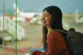 Young happy and excited Asian Korean student woman with backpack at airport departure lounge watching aircraft through glass Royalty Free Stock Photo