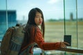 Young happy and excited Asian Korean student woman with backpack at airport departure lounge watching aircraft through glass Royalty Free Stock Photo