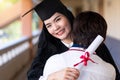 Young happy excited Asian woman university graduates in graduation gown and cap with a degree certificate hugs a friend to Royalty Free Stock Photo
