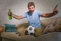 Young happy excited and crazy football fan man holding soccer ball celebrating team scoring goal and victory watching game on tele