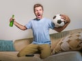 Young happy excited and crazy football fan man holding soccer ball celebrating team scoring goal and victory watching game on tele