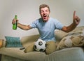 Young happy excited and crazy football fan man holding soccer ball celebrating team scoring goal and victory watching game on tele