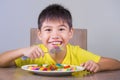 Young happy and excited male kid smiling cheerful eating dish full of candy and lollipop sitting at table isolated on grey Royalty Free Stock Photo