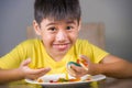 Young happy and excited male kid smiling cheerful eating dish full of candy and lollipop sitting at table isolated on grey Royalty Free Stock Photo