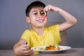 Young happy and excited male kid smiling cheerful eating dish full of candy and lollipop sitting at table isolated on grey Royalty Free Stock Photo