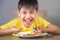 Young happy and excited male kid smiling cheerful eating dish full of candy and lollipop sitting at table isolated on grey Royalty Free Stock Photo