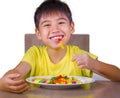 Young happy and excited male kid smiling cheerful eating dish full of candy and lollipop sitting at table isolated on white Royalty Free Stock Photo