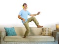 Young happy and excited man jumping on sofa couch listening to music with mobile phone and headphones playing air guitar crazy hav Royalty Free Stock Photo