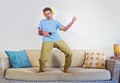 Young happy and excited man jumping on sofa couch listening to music with mobile phone and headphones playing air guitar crazy hav Royalty Free Stock Photo