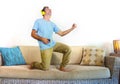 Young happy and excited man jumping on sofa couch listening to music with mobile phone and headphones playing air guitar crazy hav Royalty Free Stock Photo