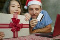 Young happy and excited mixed ethnicity couple with Asian Chinese woman and Caucasian man in Christmas Santa hat online shopping x Royalty Free Stock Photo