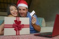 Young happy and excited mixed ethnicity couple with Asian Chinese woman and Caucasian man in Christmas Santa hat online shopping x Royalty Free Stock Photo