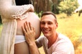 Young Happy Family, handsome husband kissing newborn baby through wife belly in nature. Royalty Free Stock Photo