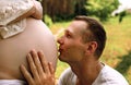 Young Happy Family, handsome husband kissing newborn baby through wife belly in nature. Royalty Free Stock Photo