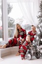 Young happy family in the same pyjamas: smiling mom, dad are sitting on big window, baby boy playing with toy retro car Royalty Free Stock Photo