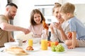 Young happy family with two cute little kids having breakfast together in kitchen and smiling Royalty Free Stock Photo