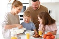 Young happy family with two cute little kids having breakfast together in kitchen and smiling Royalty Free Stock Photo