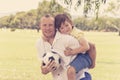 Young happy father carrying on his back excited 7 or 8 years old son playing together soccer football on city park garden posing s