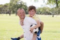Young happy father carrying on his back excited 7 or 8 years old son playing together soccer football on city park garden posing s Royalty Free Stock Photo