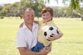 Young happy father carrying on his back excited 7 or 8 years old son playing together soccer football on city park garden posing s