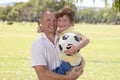 Young happy father carrying on his back excited 7 or 8 years old son playing together soccer football on city park garden posing s