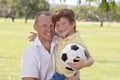 Young happy father carrying on his back excited 7 or 8 years old son playing together soccer football on city park garden posing s Royalty Free Stock Photo