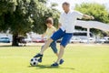 Young happy father and excited little 7 or 8 years old son playing together soccer football on city park garden running on grass k