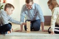 Young happy father playing with his two cute children with wooden blocks