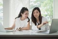Young happy friends working in office. Two beautiful Asian woman sitting in office with laptop and document paper chart on desk. Royalty Free Stock Photo