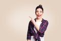 Young happy girl with casual style and bun hair pointing her finger sideways, demonstrating something on beige blank wall Royalty Free Stock Photo