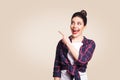 Young happy girl with casual style and bun hair pointing her finger sideways, demonstrating something on beige blank wall Royalty Free Stock Photo