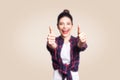 Young happy girl with casual style and bun hair thumbs up her finger, on beige blank wall with copy space looking at camera Royalty Free Stock Photo