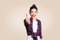 Young happy girl with casual style and bun hair thumbs up her finger, on beige blank wall with copy space looking at camera Royalty Free Stock Photo