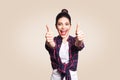 Young happy girl with casual style and bun hair thumbs up her finger, on beige blank wall with copy space looking at camera with t Royalty Free Stock Photo