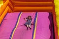 Young happy girl child in dress riding inflatable slide outdoors a warm summer day. Royalty Free Stock Photo