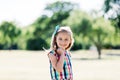 A young happy girl in colorful checkered dress standing in the park,