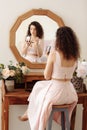 Young happy girl with curly hair does makeup in front of a vintage mirror. A beautiful woman in a pink dress paints her eyes Royalty Free Stock Photo