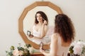 Young happy girl with curly hair does makeup in front of a vintage mirror. A beautiful woman in a pink dress paints her eyes Royalty Free Stock Photo